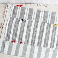 2: A madras stripe placemat in multicolor with tassel detail.