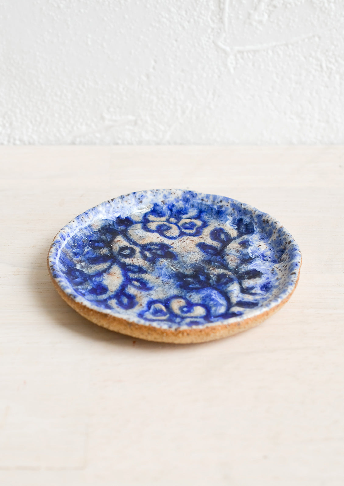 A round ceramic dish with floral imprint and blue glaze.