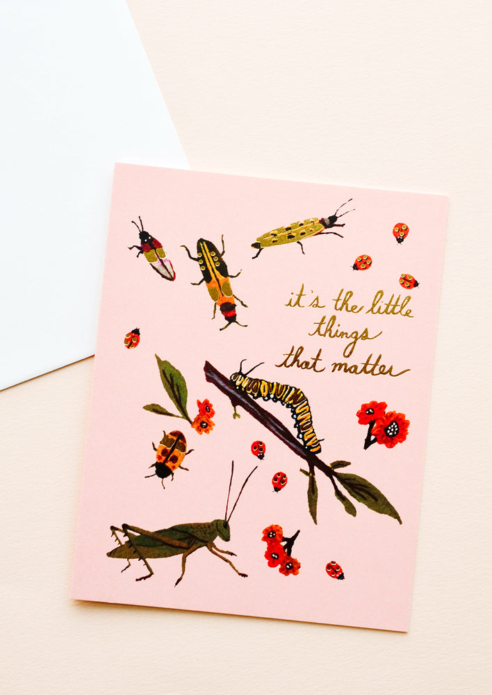 1: Pink greeting card with ladybugs, insects and flowers and gold text reading "It's the little things that matter"