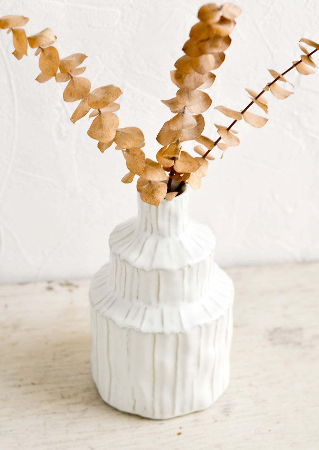 1: A textured white vase in an asymmetrical shape with dried eucalyptus.