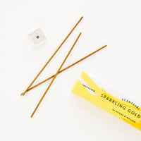 Gold Yuzu: Three thin incense sticks laid out next to a small square holder and yellow cardboard box.