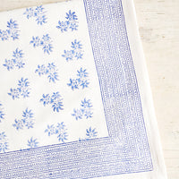 1: White cotton tablecloth with blue floral print, folded on an antique table.