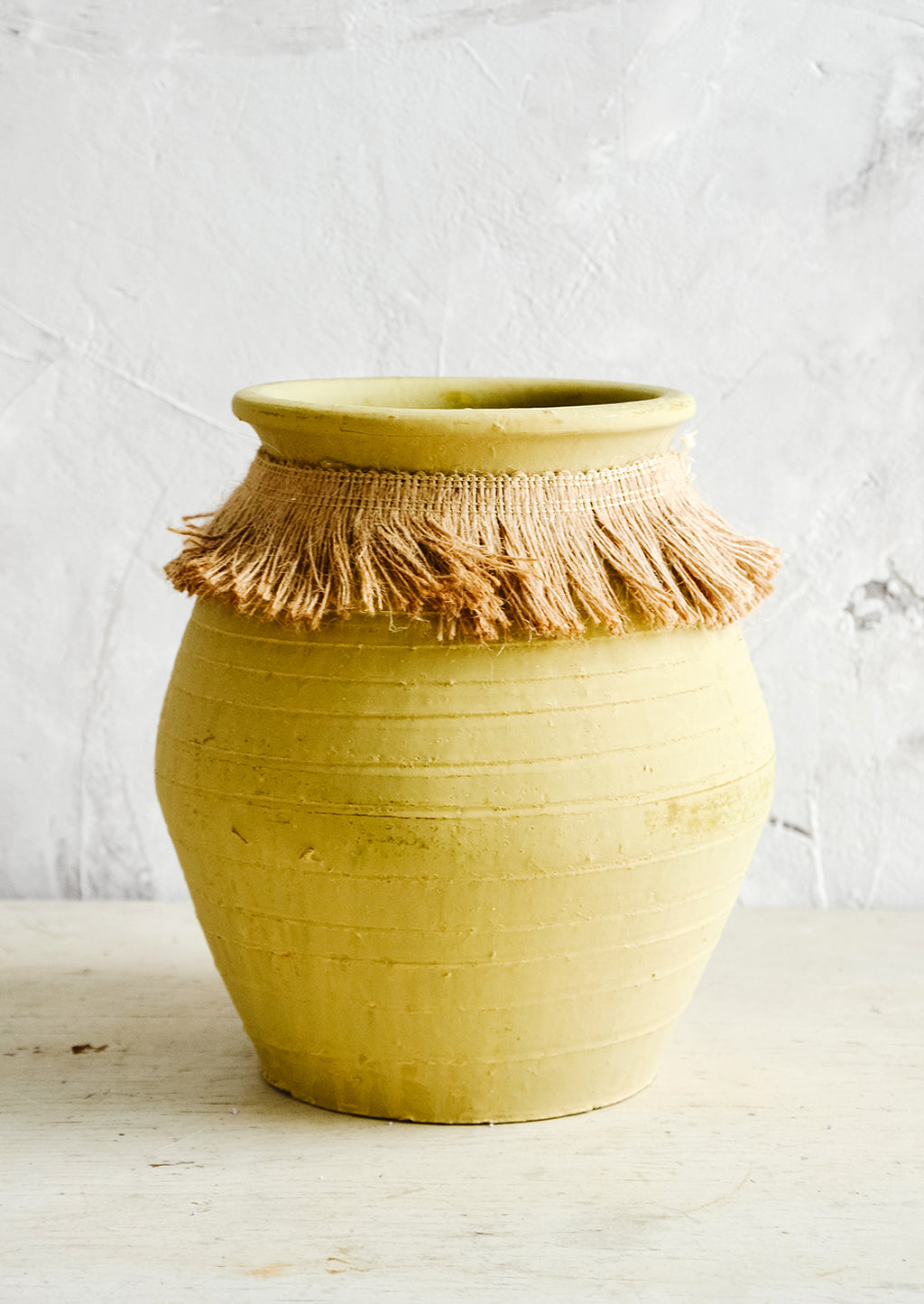 Large: Tall, ochre colored clay vase with fringed jute trim around opening