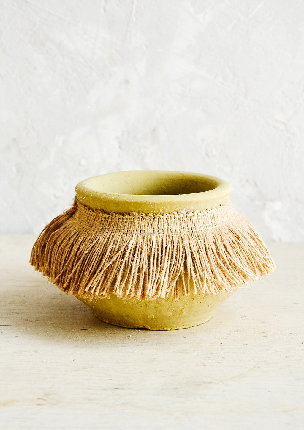 Small: Short, ochre colored clay vase with fringed jute trim around opening