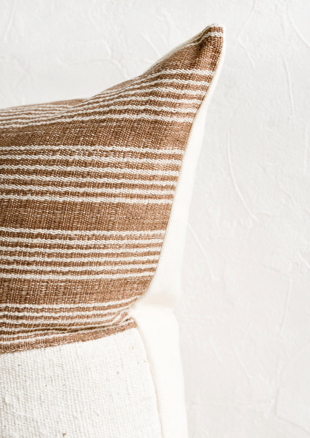 3: A throw pillow with top half in brown & ivory striped fabric and ivory linen back.