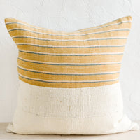 2: A throw pillow with top half in mustard, ivory & teal striped fabric and bottom half in natural mudcloth.
