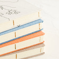 5: A stack of cloth journals with hand-bound seams.