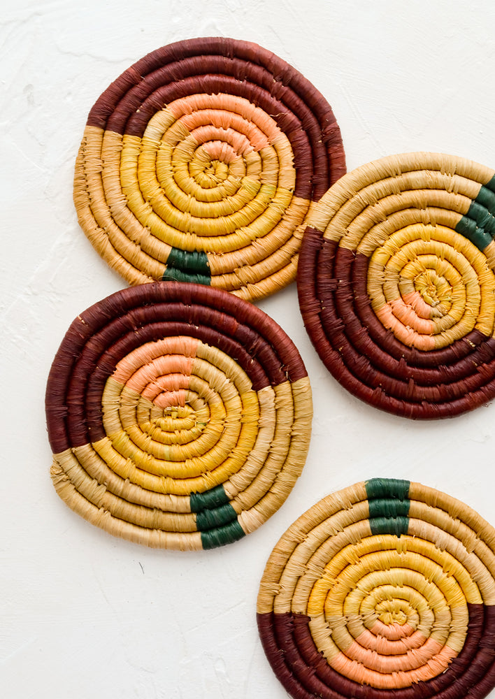 Four round woven raffia coasters in colorblock multicolor design.