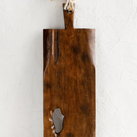 1: A rectangular wooden cutting board with knot cutout detail and twine strap handle.