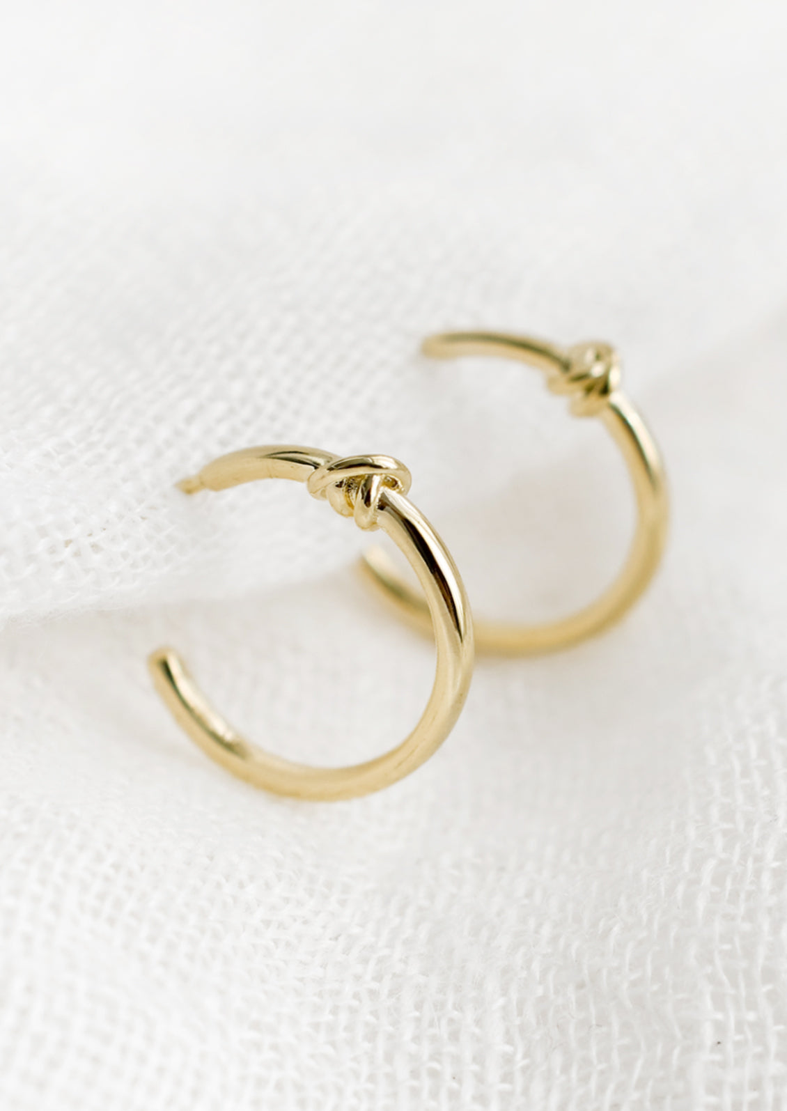A pair of gold hoop earrings with single knot detail at top.
