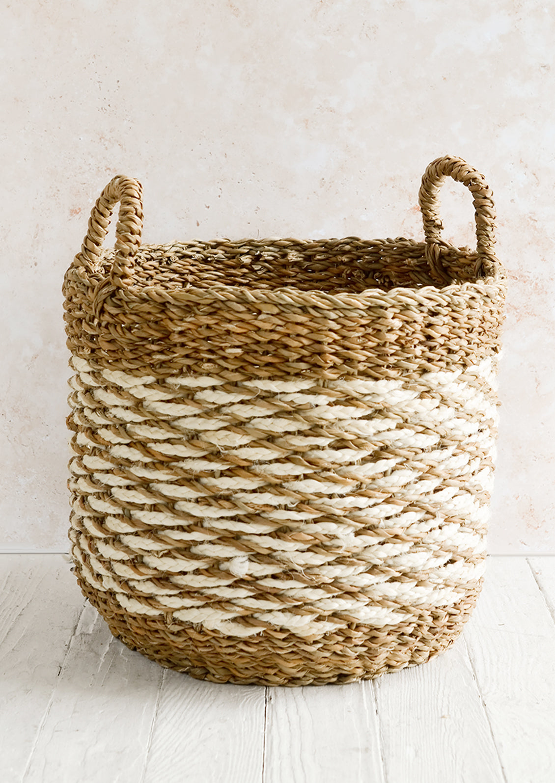 A large open-top round storage basket made from seagrass with braided jute, featuring two handles at top.