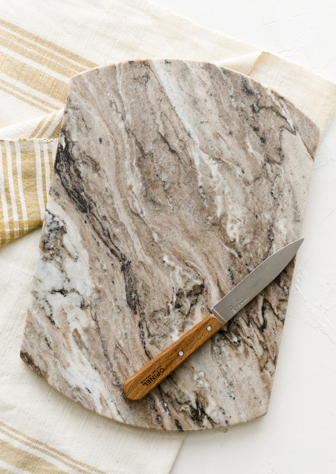 a rectangular marble serving board with rounded sides next to a hand towel and knife