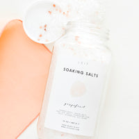 Grapefruit: An unlidded tall glass jar with a simple white and pink label and white salt crystals spilling out of it.