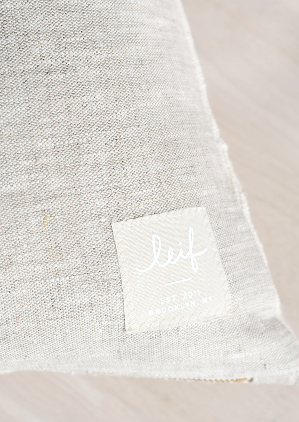 3: Natural linen with hand-stitched square logo patch at bottom corner.