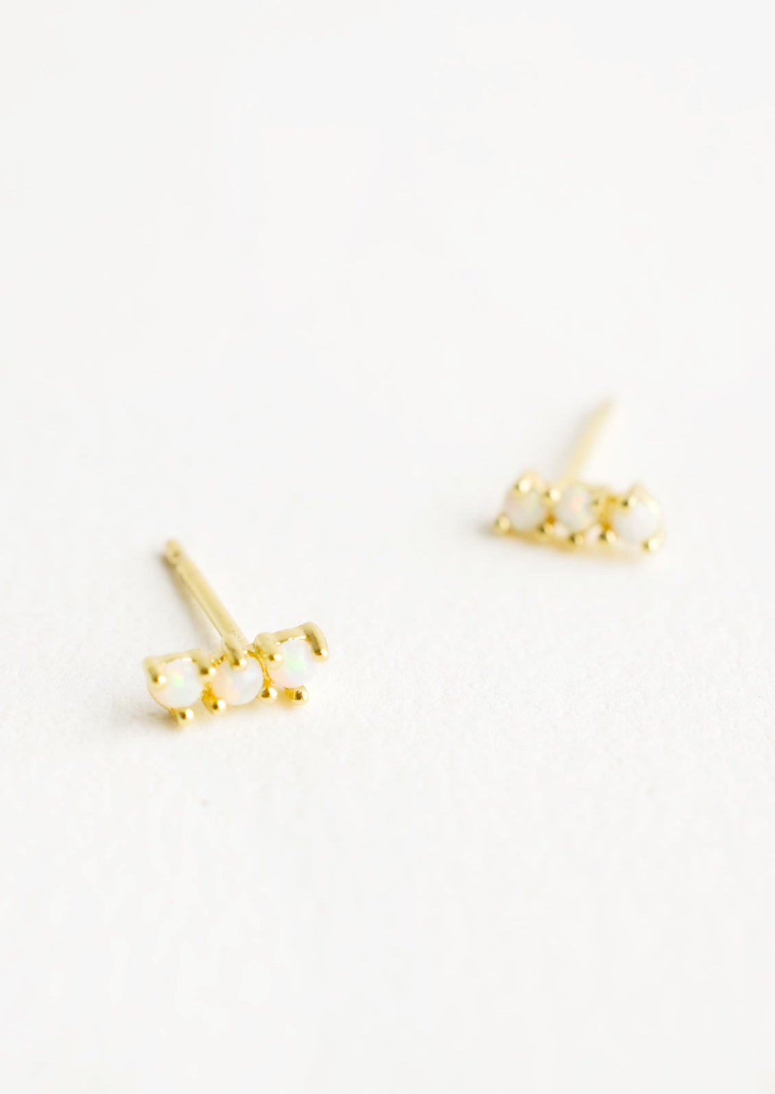 Small gold plated stud earrings with three round white opal stones stacked in a row