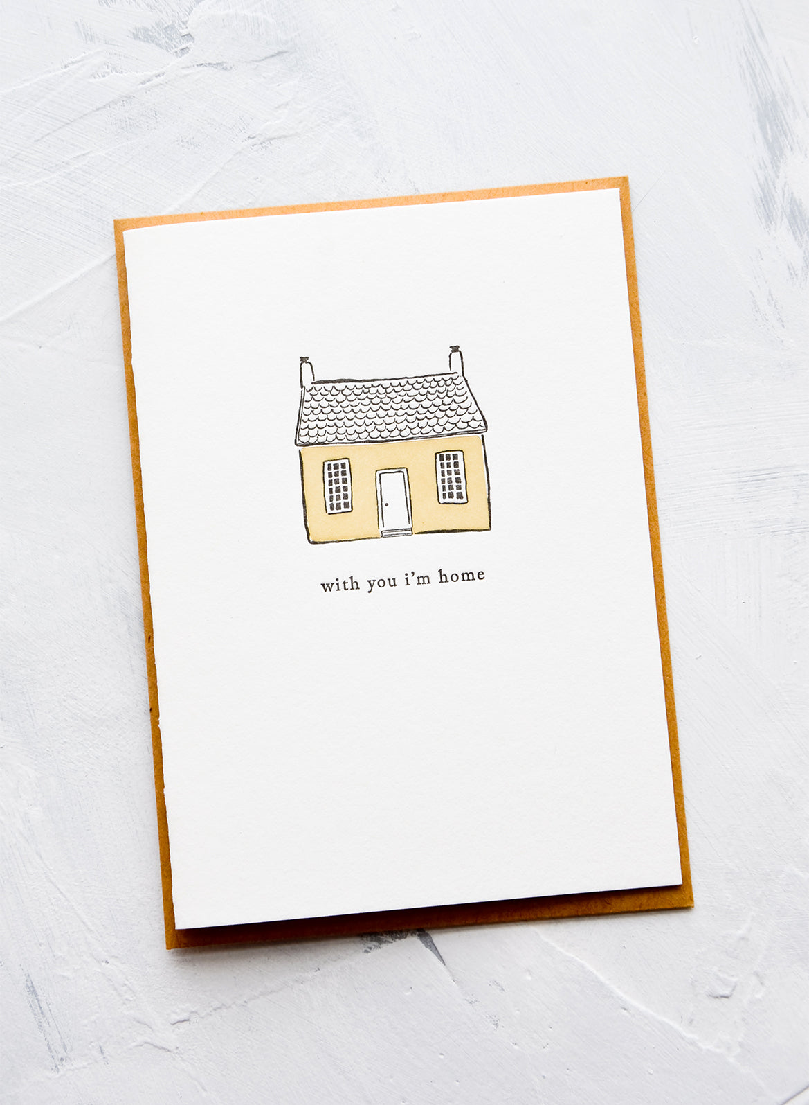 A letterpress printed greeting card with an image of a house and text underneath reads "with you i'm home"
