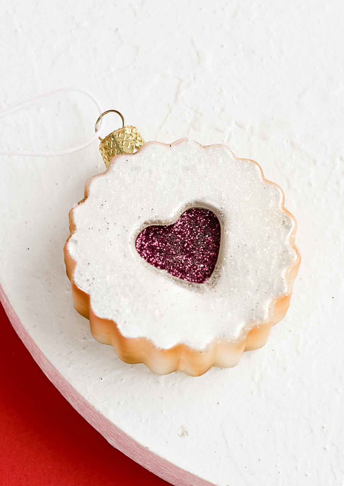 A glass holiday ornament in shape of raspberry linzer cookie with heart center.