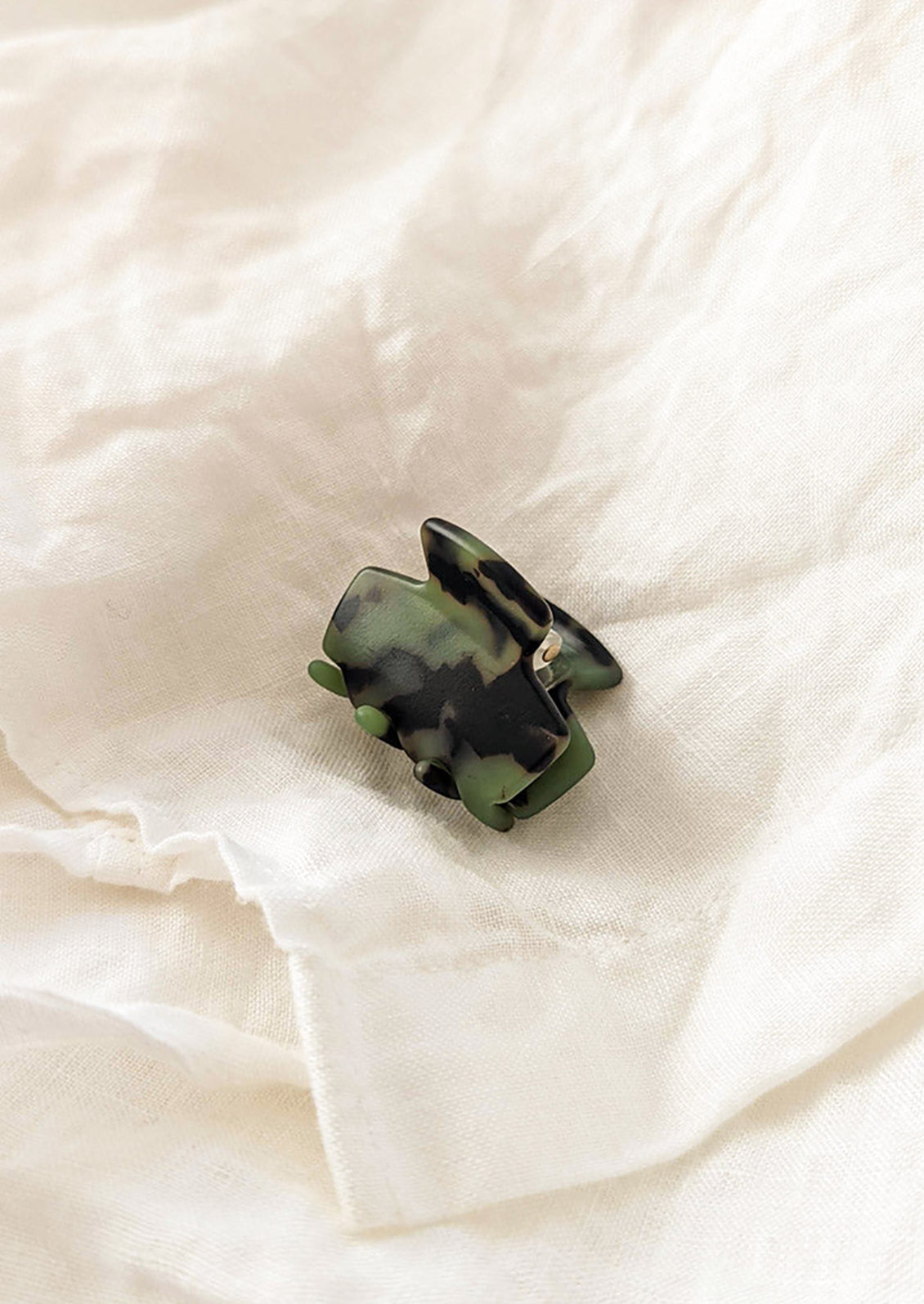 A miniature hinged hair claw in green and black tortoiseshell pattern.