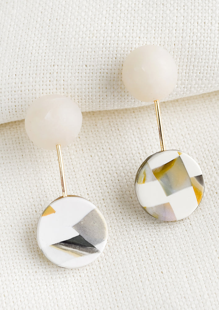 A pair of earrings with round ball connected by thin gold bar to checkered circle.