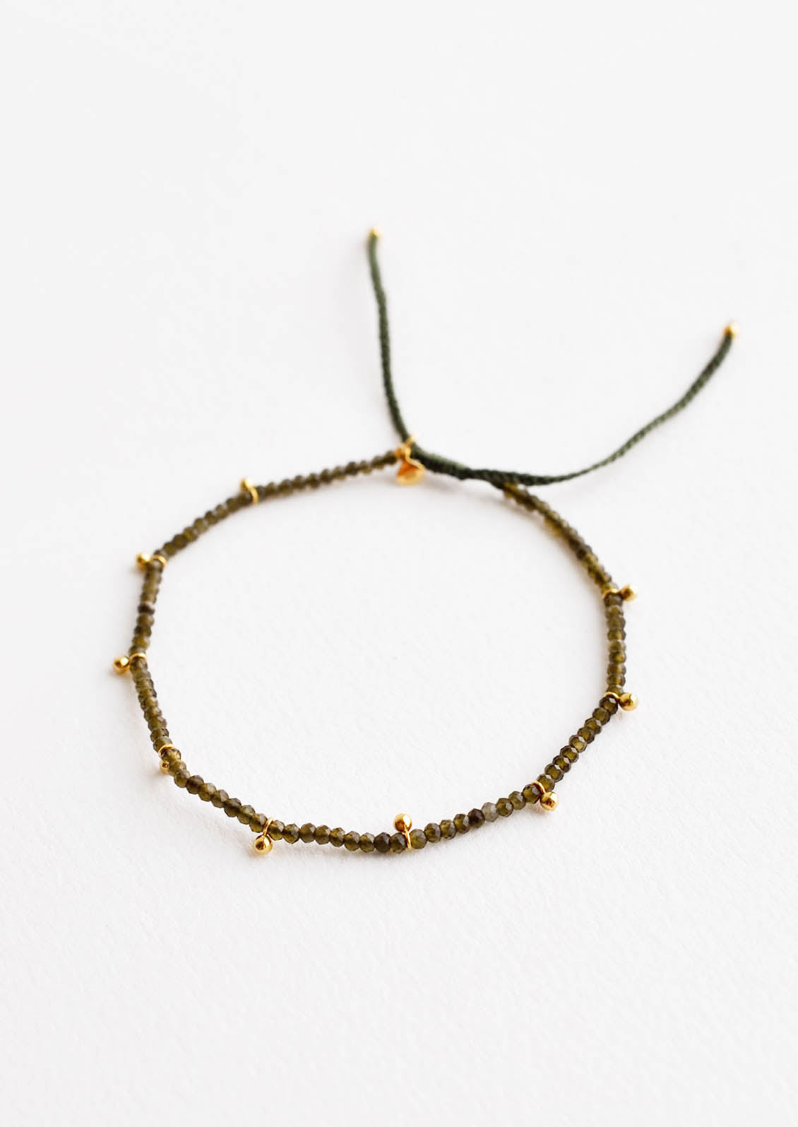 A bracelet of small green gemstones and evenly spaced gold beads.