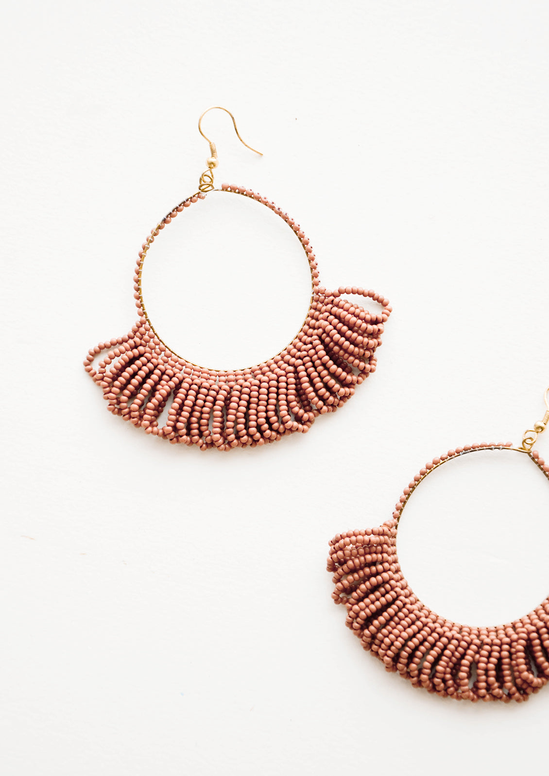 Dangling hoop earrings featuring clay red beads and accented with hanging beaded, looped fringe.