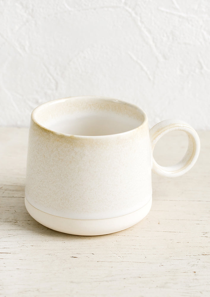 A ceramic mug in ivory and white with round circular handle.