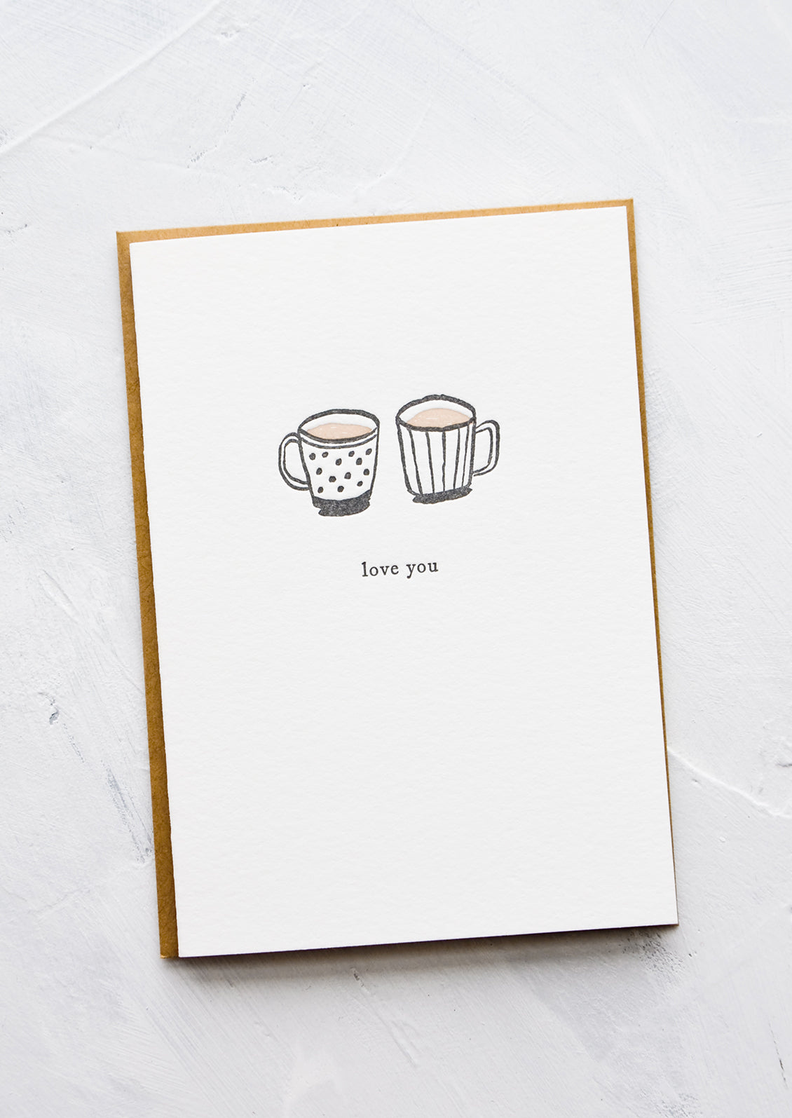 A letterpress printed greeting card with an image of two coffee mugs side by side, text below image reads "love you".