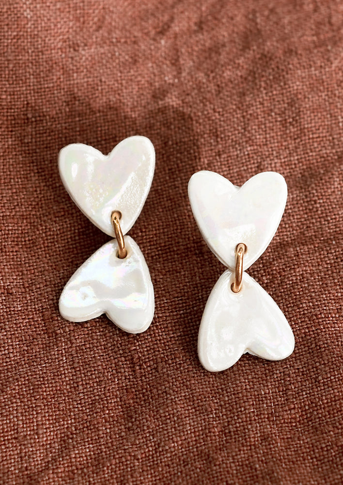 1: A pair of white pearlized ceramic earrings in shape of two hearts in opposite positioning.