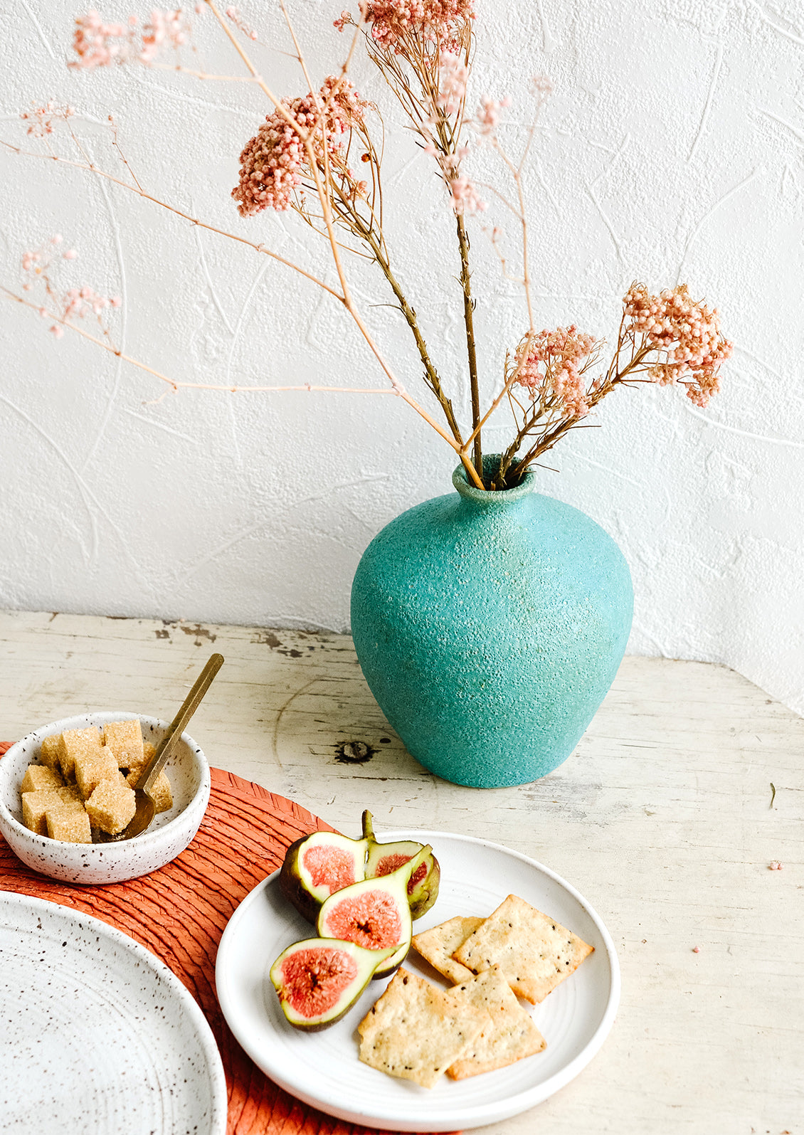 A turquoise ceramic vase amidst a breakfast tabletop scene.