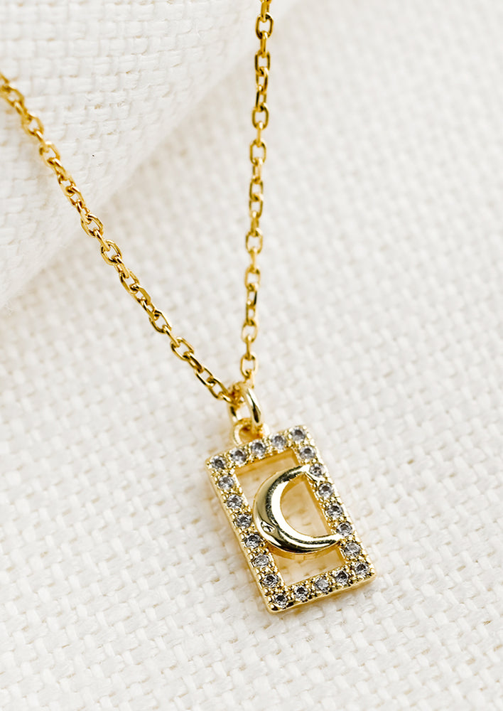 A gold necklace with rectangular framed moon charm.
