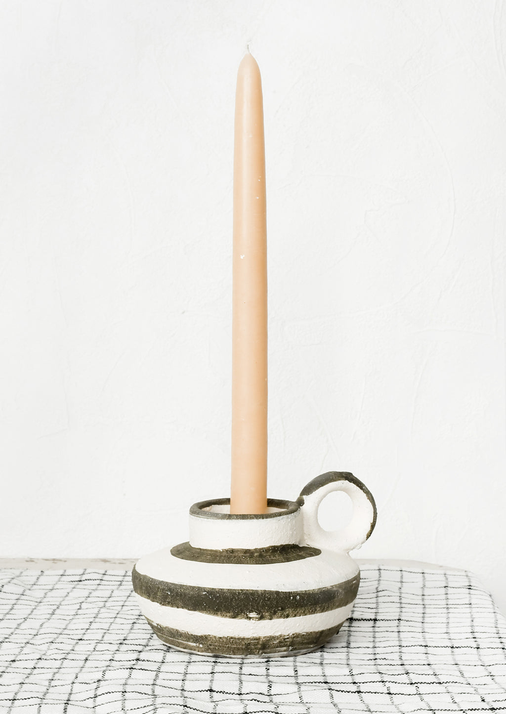 2: A black and white candle holder holding a tan colored taper candle.