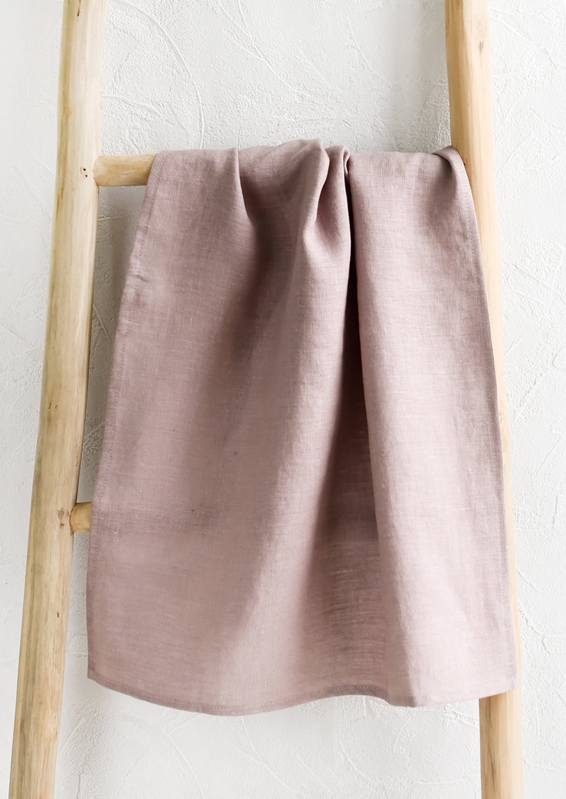 A dusty lilac linen tea towel draped on a wooden ladder.
