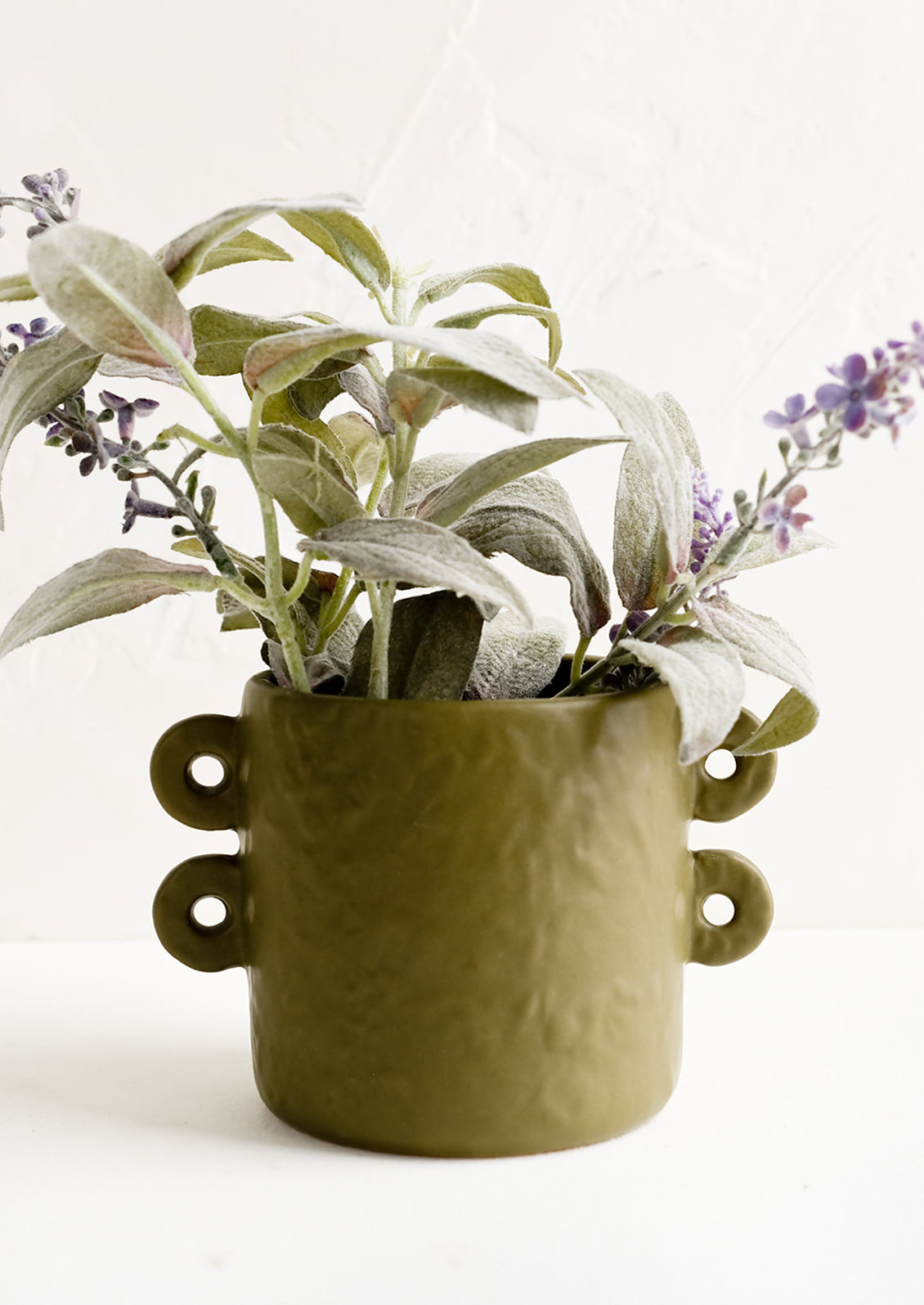 An army green round planter holding lavender plant.
