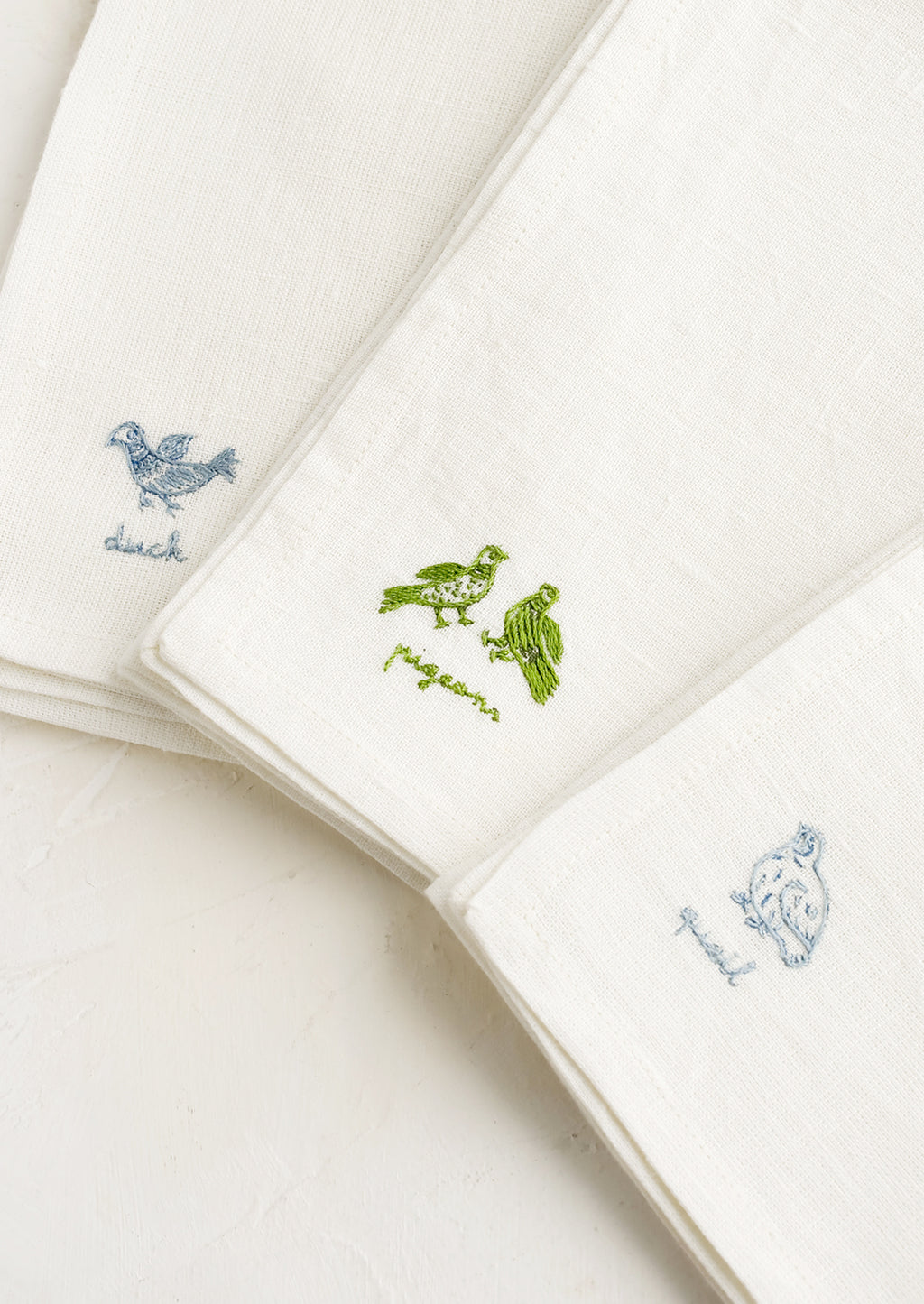 Antique Blue / Quail: White linen napkins with bird embroidery detailing.