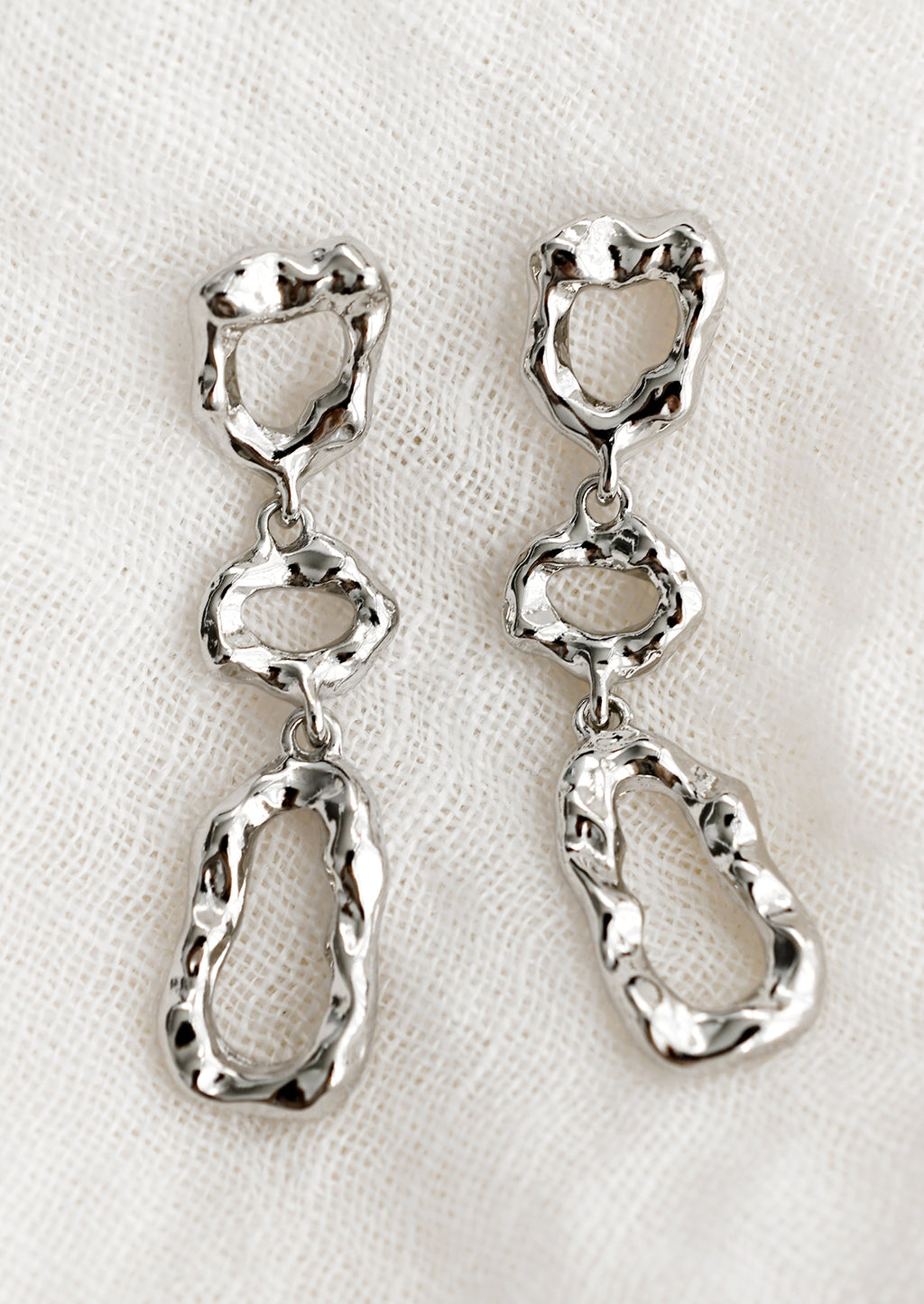Silver: A pair of silver abstract shape drop earrings with melted metal look.