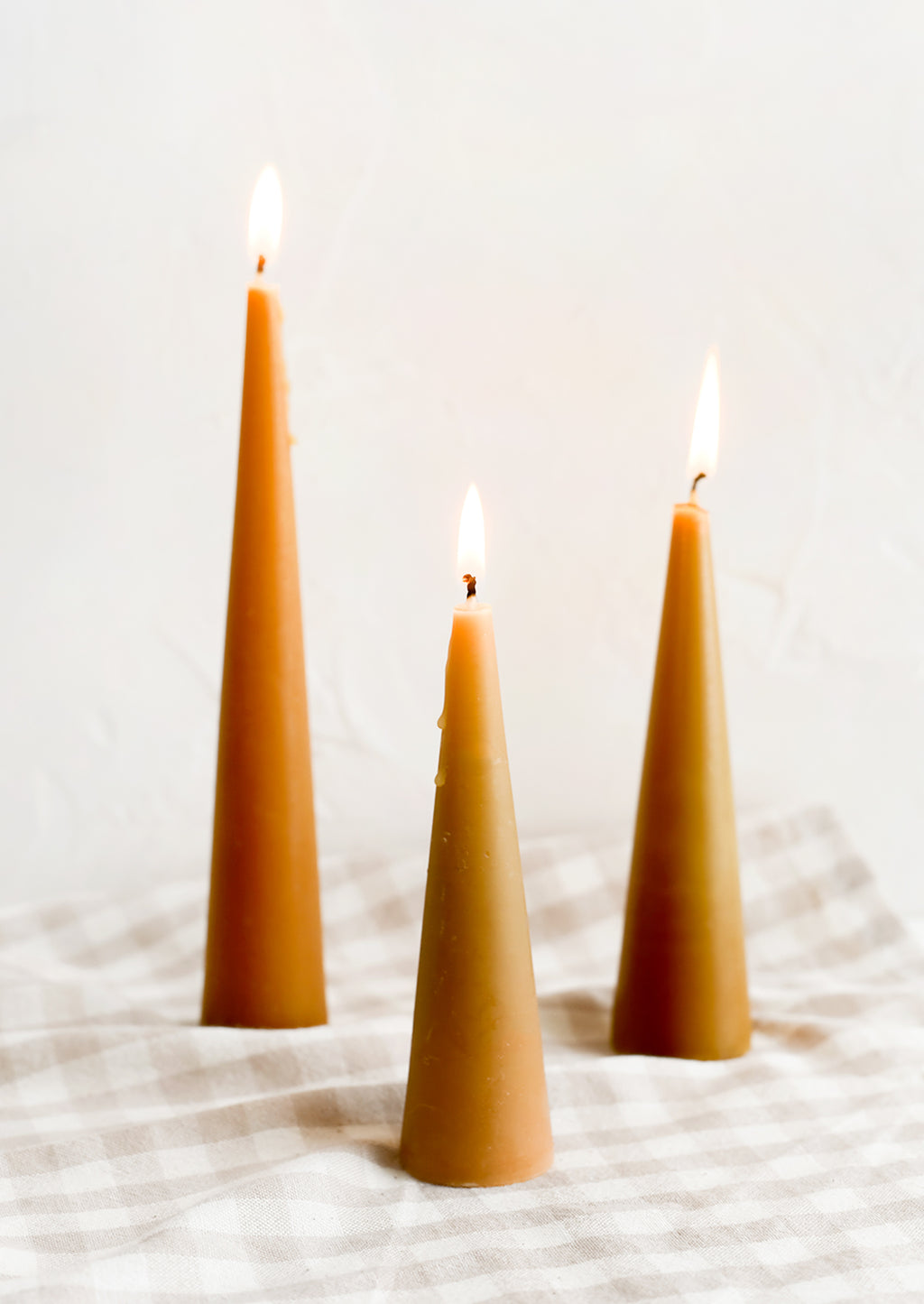 Small / Caramel: Three lit cone-shaped taper candles in caramel.