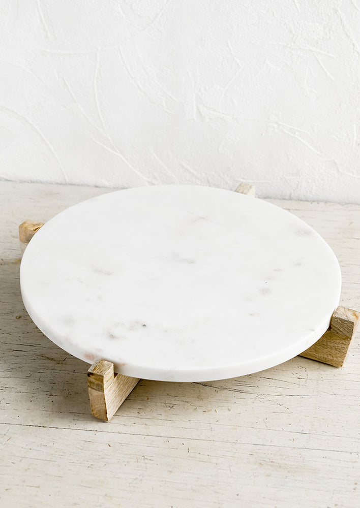 1: A round white marble riser on wooden X stand.