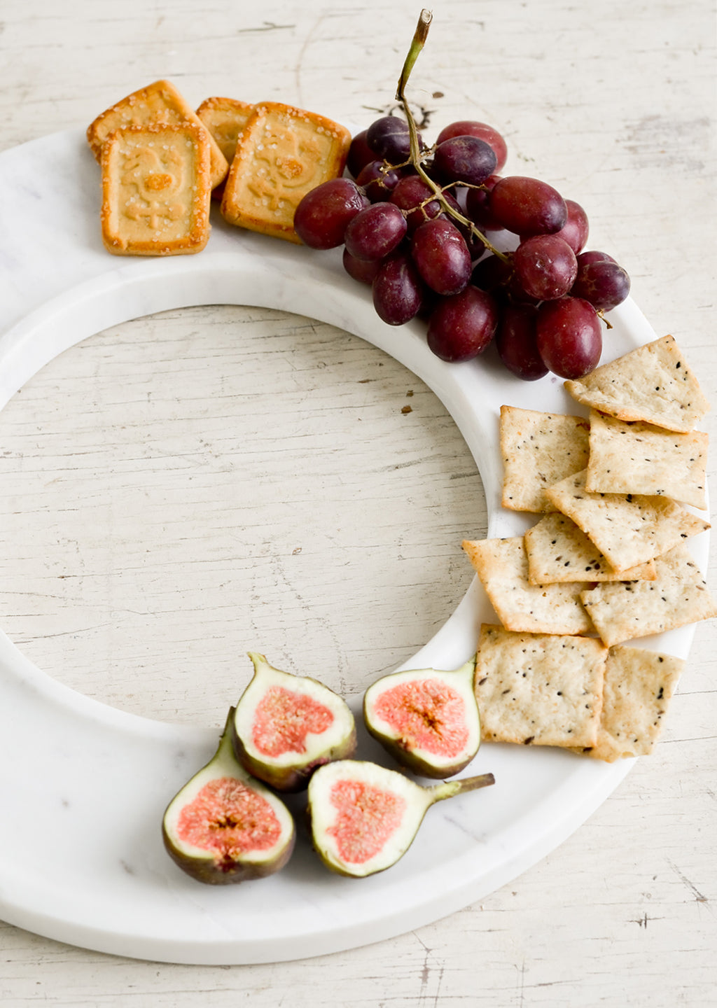 2: A circular white marble tray covered in crackers, grapes & figs.