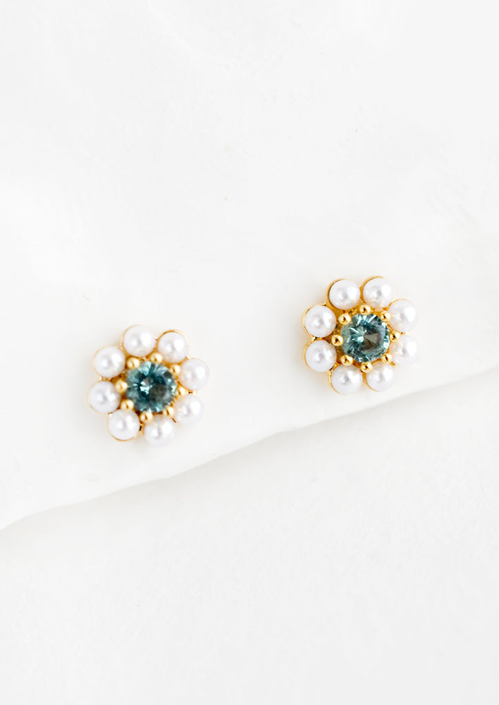 A pair of gold stud earrings in the shape of a flower made from pearls with blue crystal center.