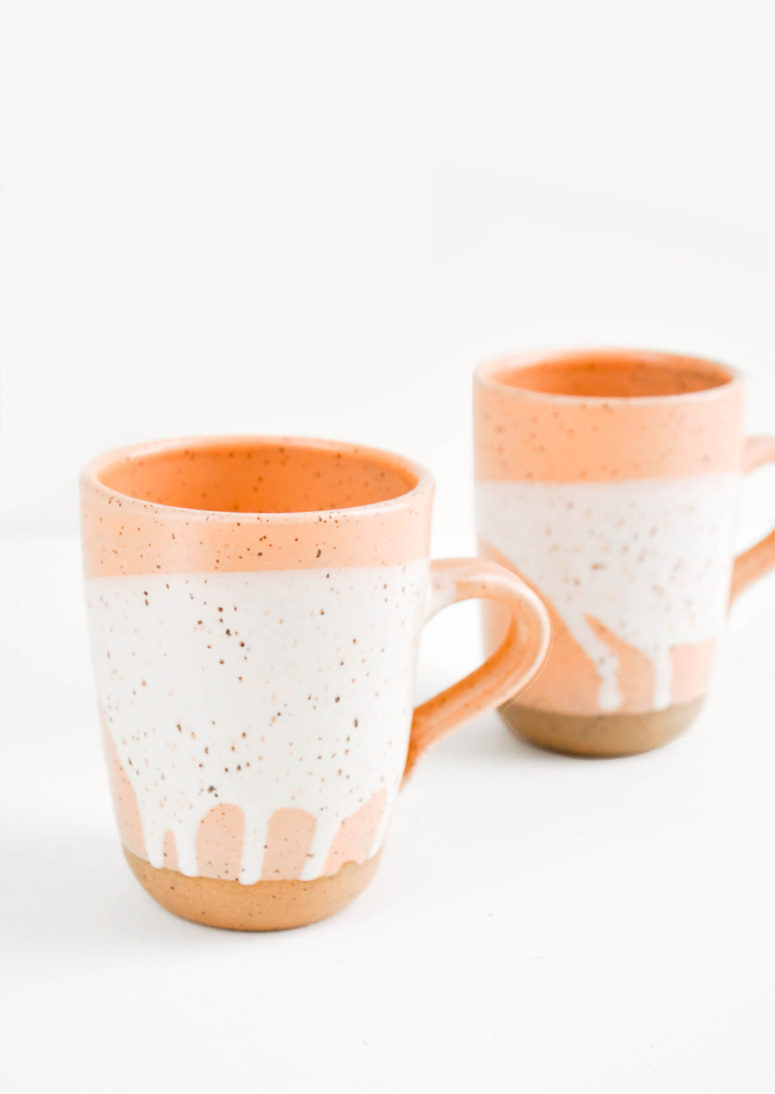 Two ceramic mugs in orange and white with brown speckles.