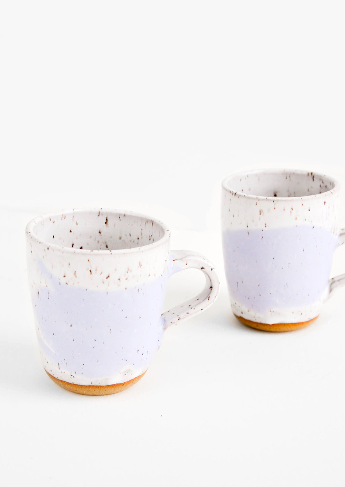 Two ceramic mugs in white and purple with brown speckles.