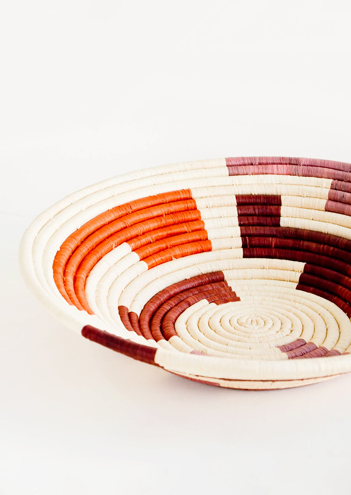 Shallow woven raffia bowl with maze print in wine, orange and mauve