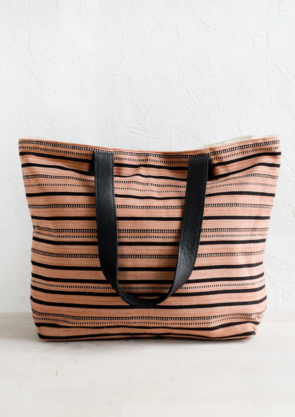 A striped canvas tote bag with black leather handles.