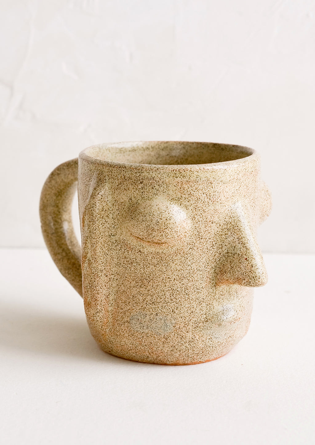 Natural: A clay mug in speckled sand color in face shape.