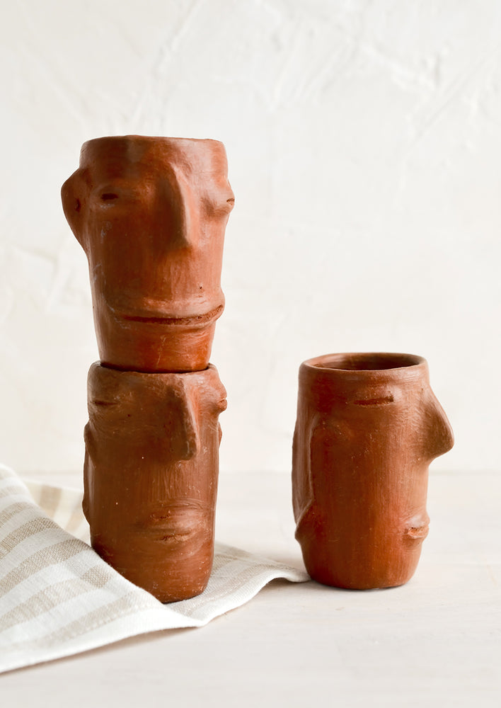 1: Handmade shot glasses made from red clay showing unique, primitive faces on them.