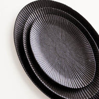 2: Oval-shaped, black ceramic trays with radiating lines pattern stacked in incremental sizes