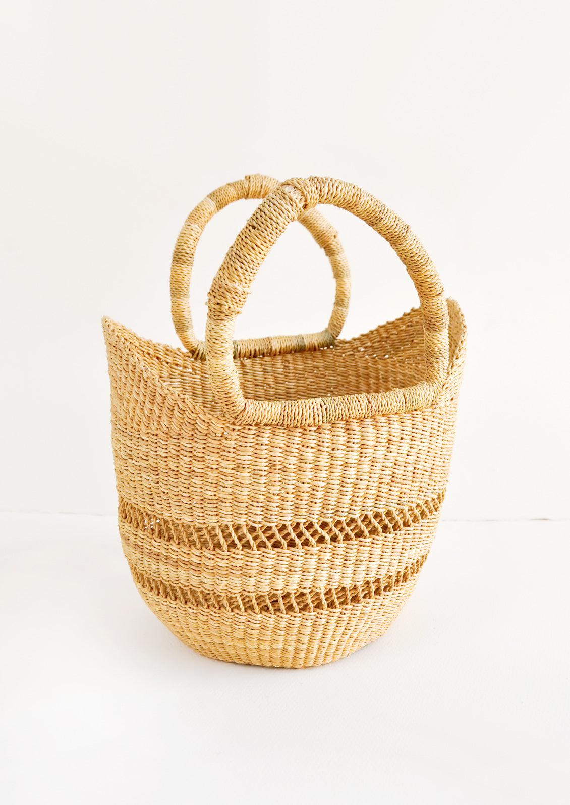Petite decorative basket woven from natural grass, with two handles at top. Features an airy, open weave stripe detail.