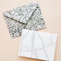 2: An envelope patterned with green and gray paint splatter and a white greeting cards with thin strokes of gray paint.