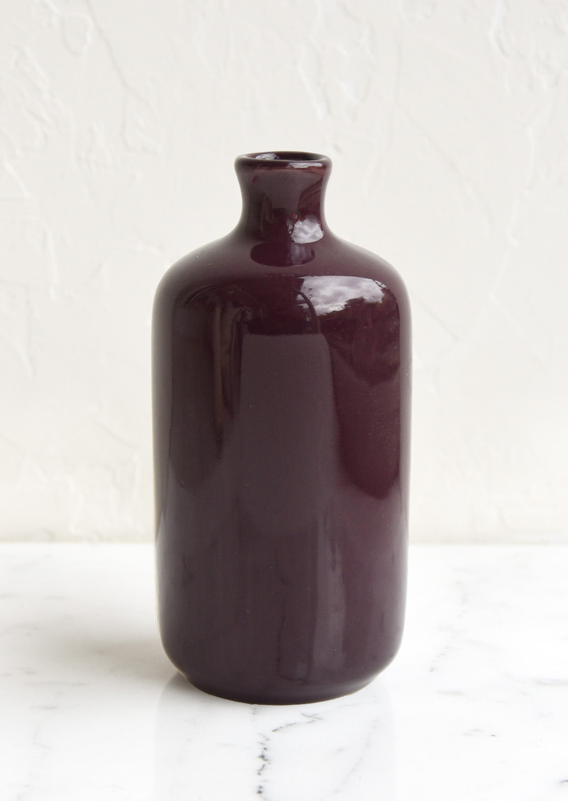 A ceramic bud vase in tall shape, dark purple color.