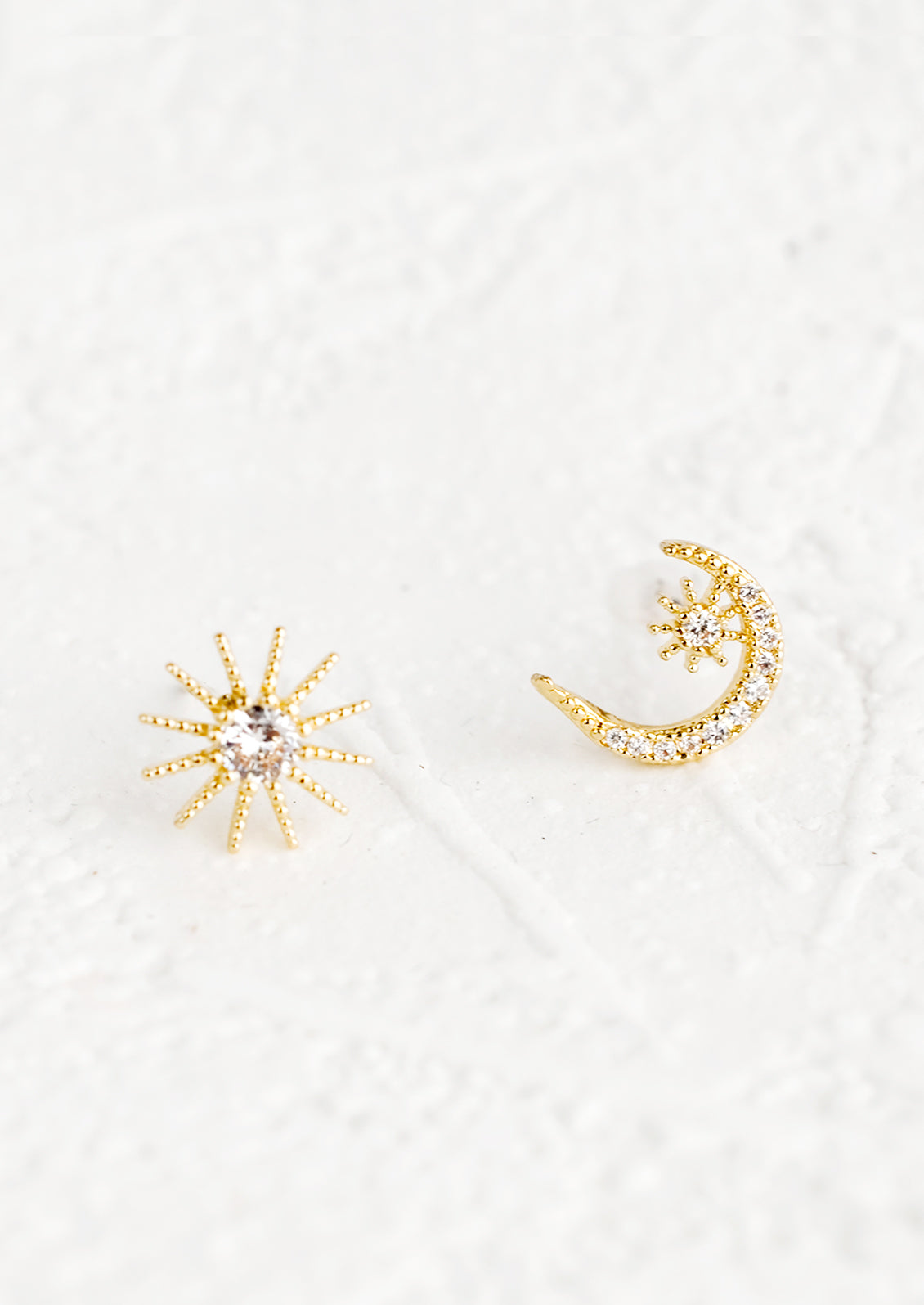 A pair of mismatched stud earrings, one piece is a sun and one piece is a moon.